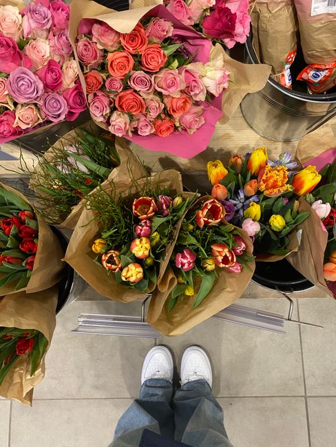 A selection of fresh floral bouquets displayed on a tiled floor inside a flower shop. The arrangements include a large bouquet of pale pink, lavender, and coral roses wrapped in pink paper, and multip
